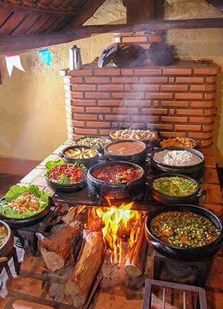 Rustic kitchen with a brick stove and multiple black pots cooking over a fire.