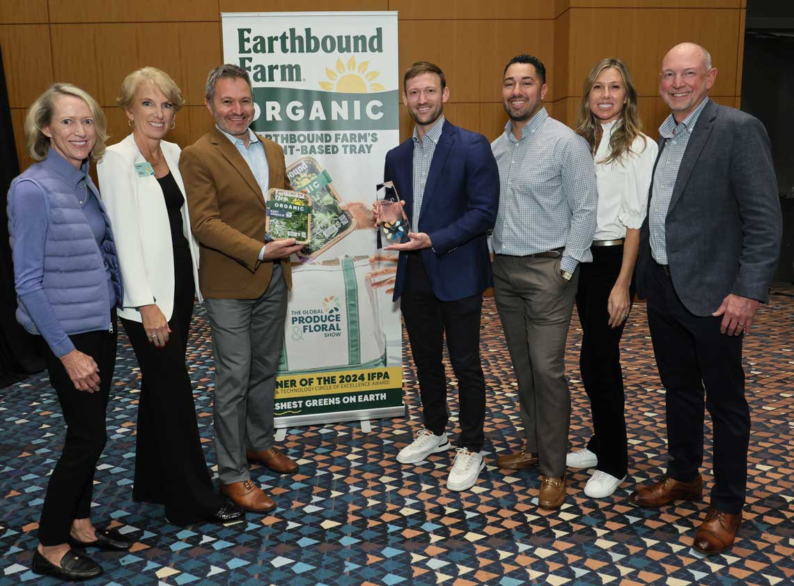 A group of seven people poses with Earthbound Farm Organic products and award in front of a branded banner.