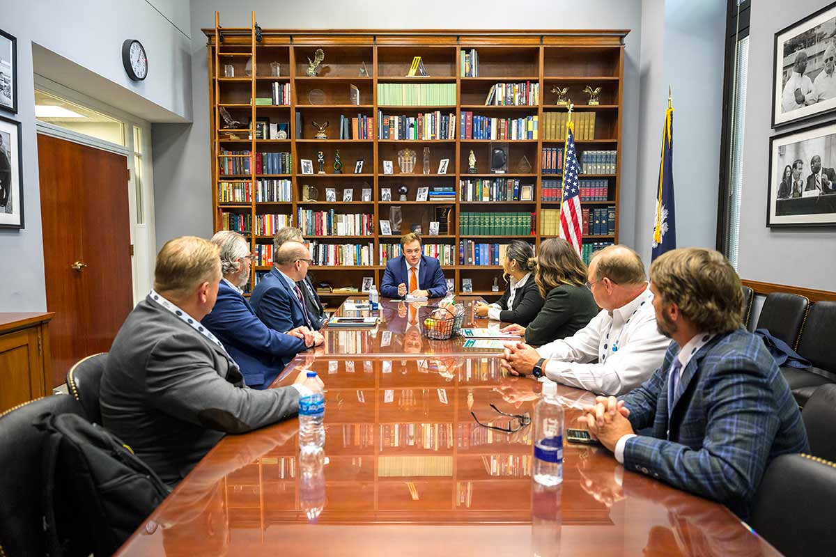 Nine Washington Conference attendees sit around a conference table in discussion. The walls are covered with full bookcases.