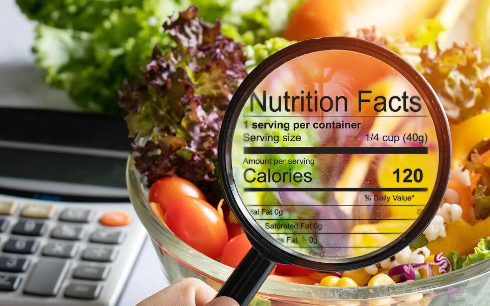 Hand holding magnifying glass over a bowl of salad with the nutrition information of the salad showing in the glass