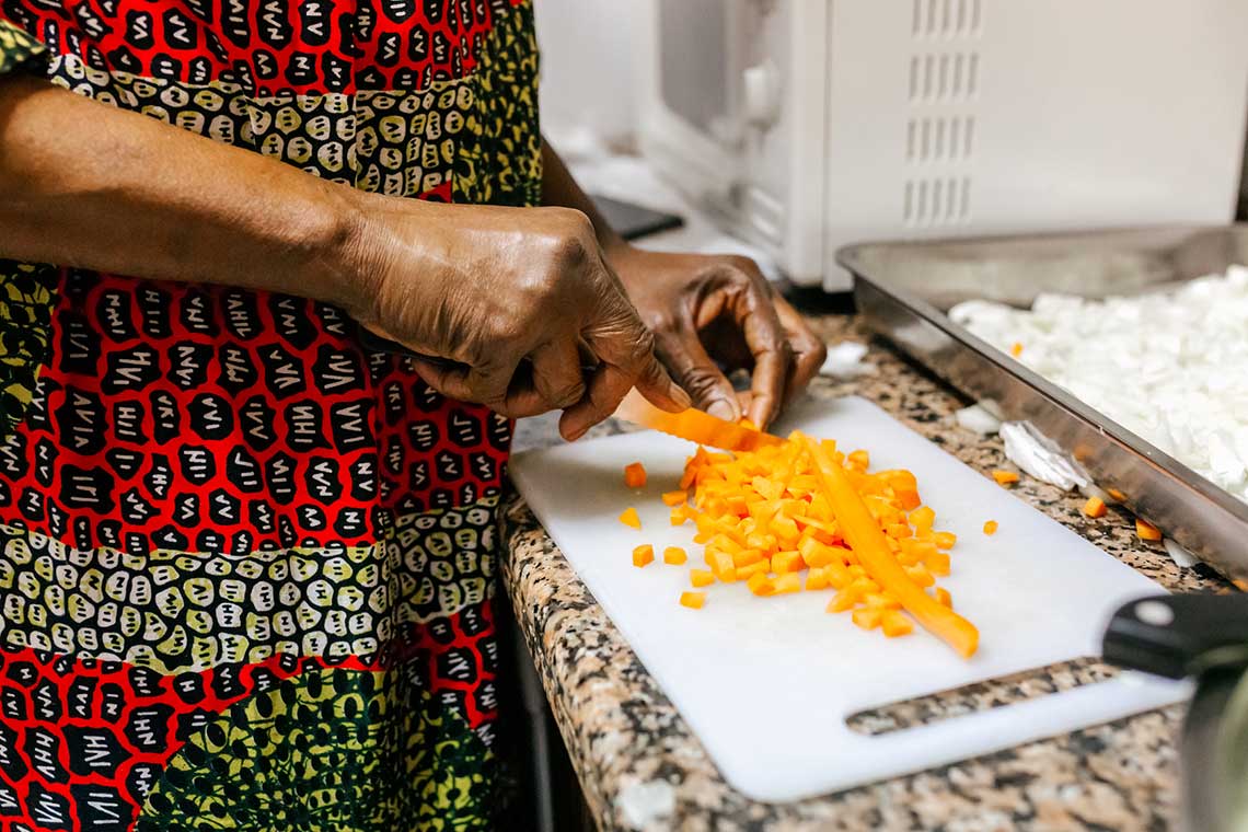 Person chopping carrots on a white cutting board in a kitchen.