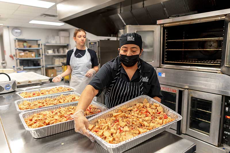 A group of women from DC Central Kitchen prepare strawberry French toast in a school cafeteria kitchen